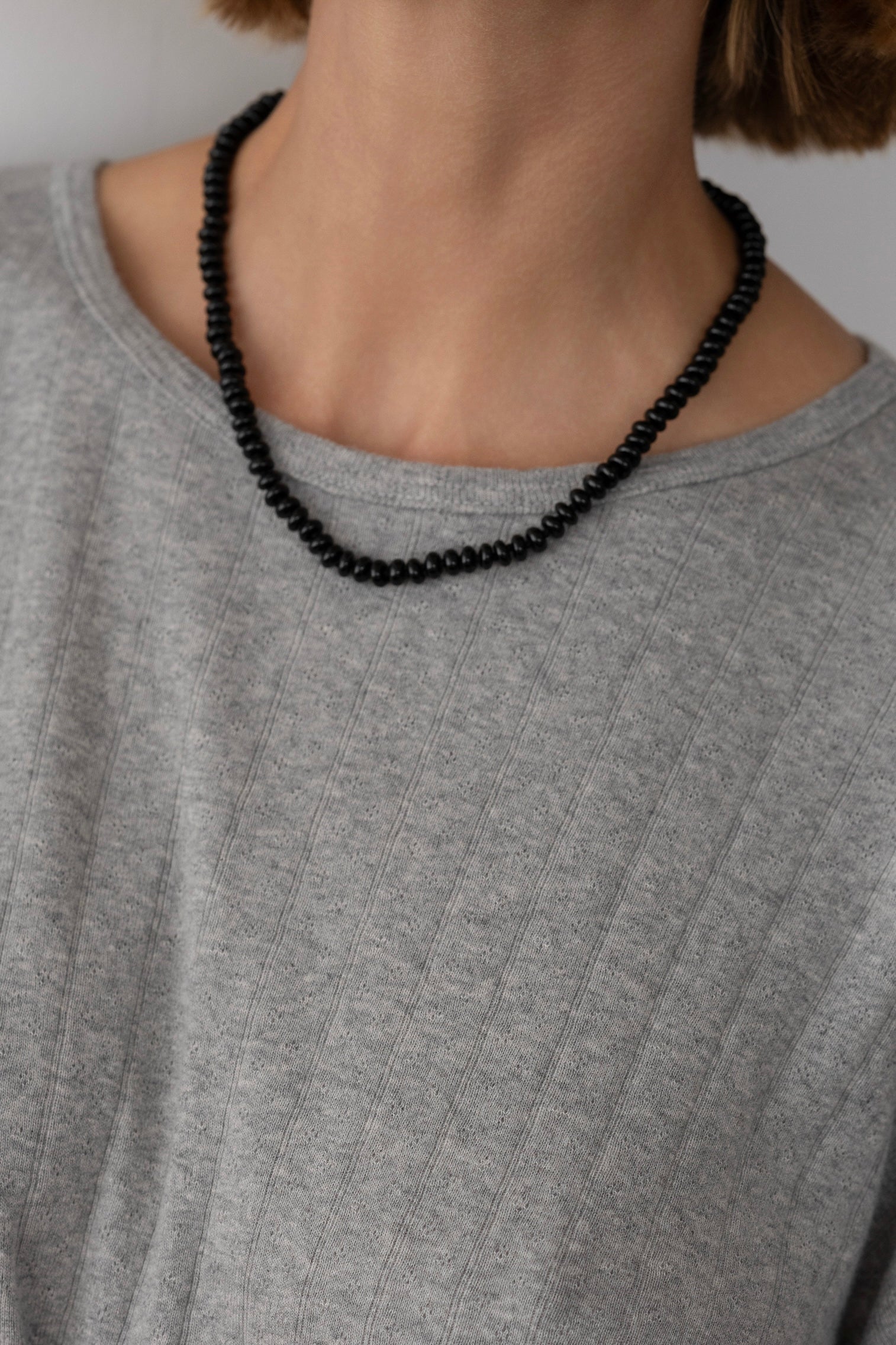 Person wearing a black beaded necklace against a neutral background