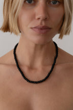 Person wearing a black beaded necklace against a neutral background