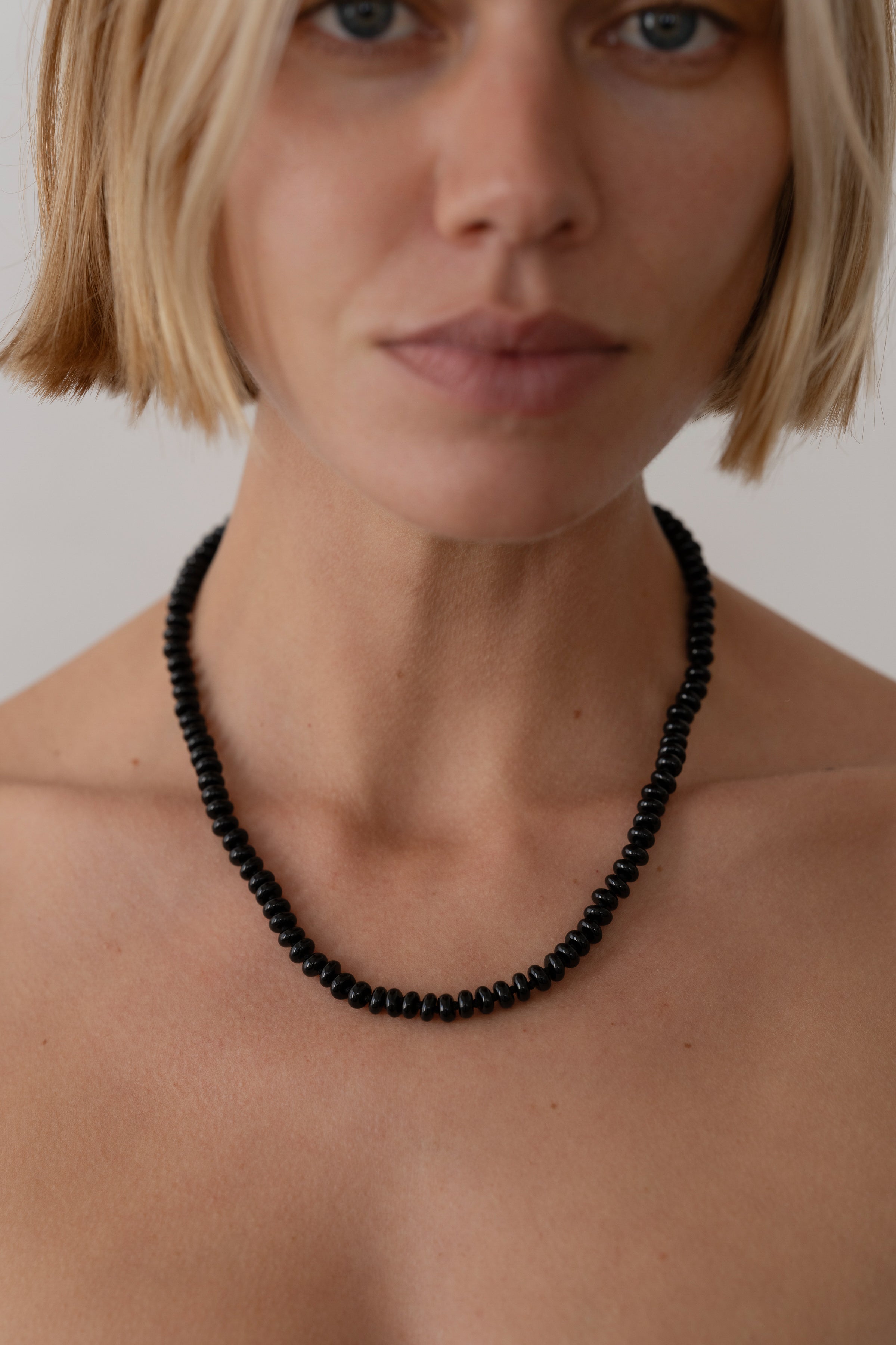 Person wearing a black beaded necklace against a neutral background
