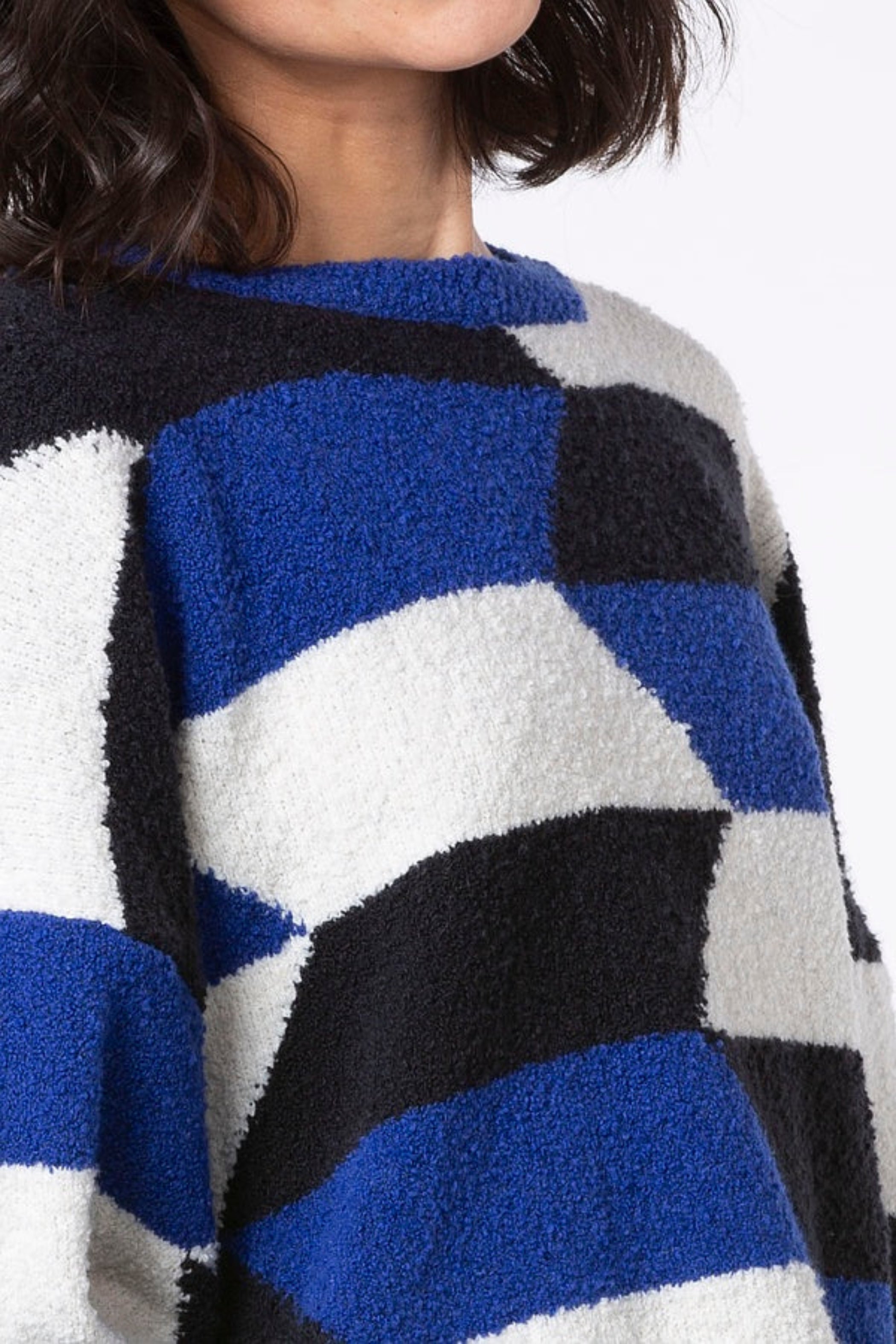 Women's cropped long sleeve pullover made from a boucle yarn knit from Oska. In geometric blue, black, and white pattern. Detail view.