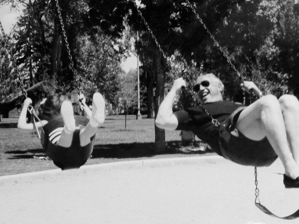 Black and white image of two people swinging in a park