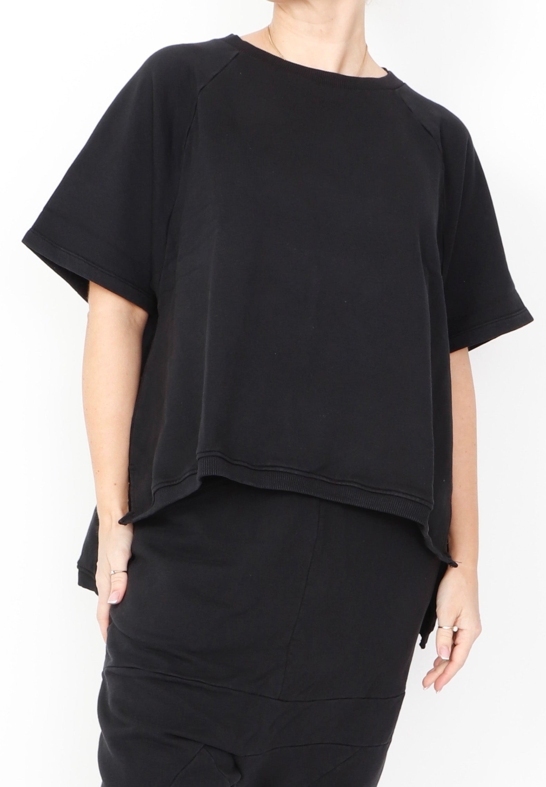 Women's short Ragland sleeve relaxed top, with a hi -low cut with 7" slits at the sides. Made in an organic cotton French Terry fabric from Sort Aarhus. In colour black. Front view.