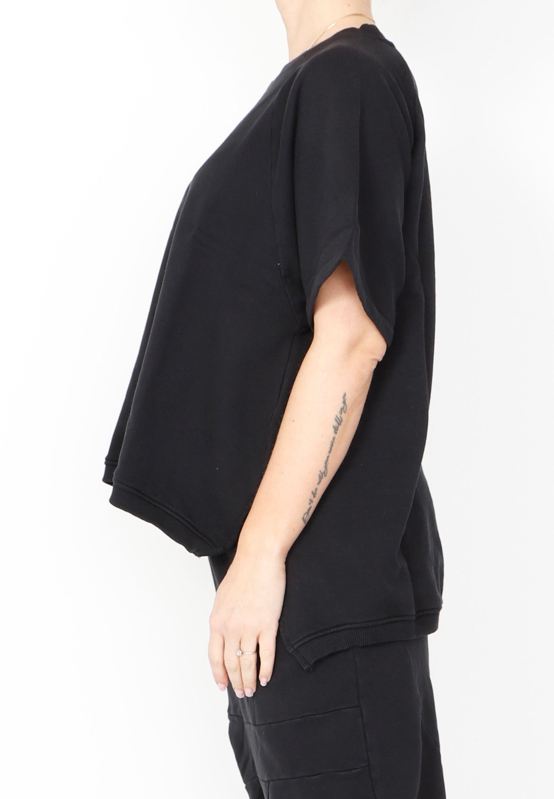 Women's short Ragland sleeve relaxed top, with a hi -low cut with 7" slits at the sides. Made in an organic cotton French Terry fabric from Sort Aarhus. In colour black. Side view.