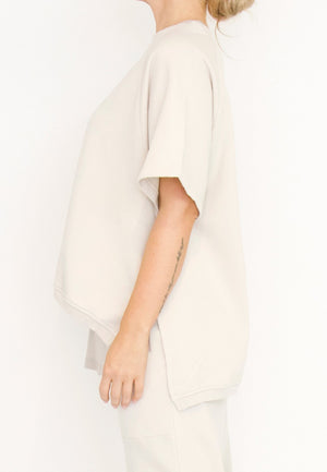 Women's short Ragland sleeve relaxed top, with a hi -low cut with 7" slits at the sides. Made in an organic cotton French Terry fabric from Sort Aarhus. In colour creme. Side view.