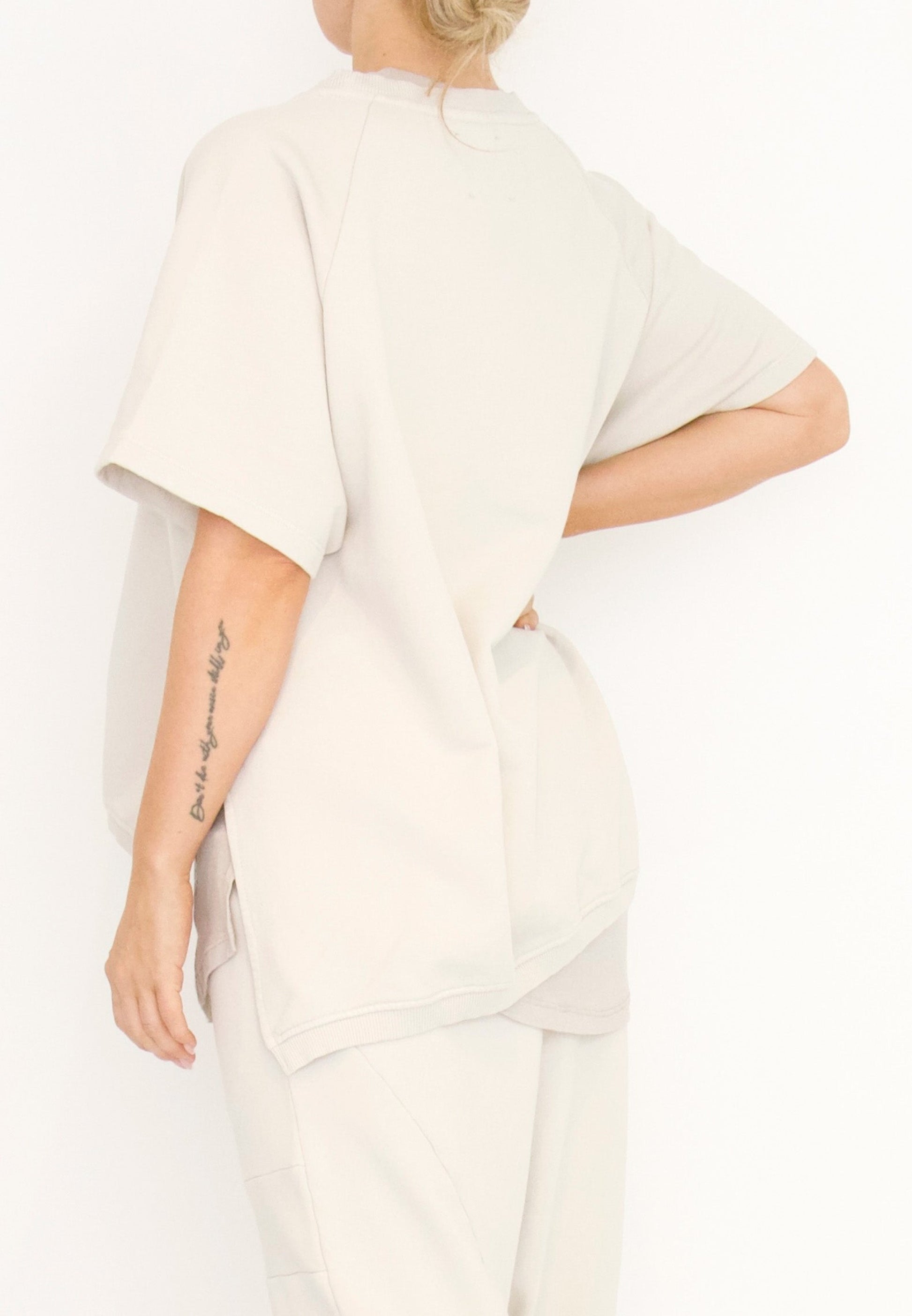 Women's short Ragland sleeve relaxed top, with a hi -low cut with 7" slits at the sides. Made in an organic cotton French Terry fabric from Sort Aarhus. In colour creme. Back view.