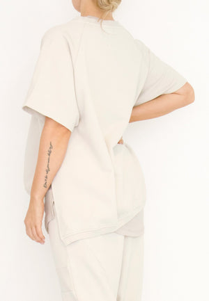 Women's short Ragland sleeve relaxed top, with a hi -low cut with 7" slits at the sides. Made in an organic cotton French Terry fabric from Sort Aarhus. In colour creme. Back view.