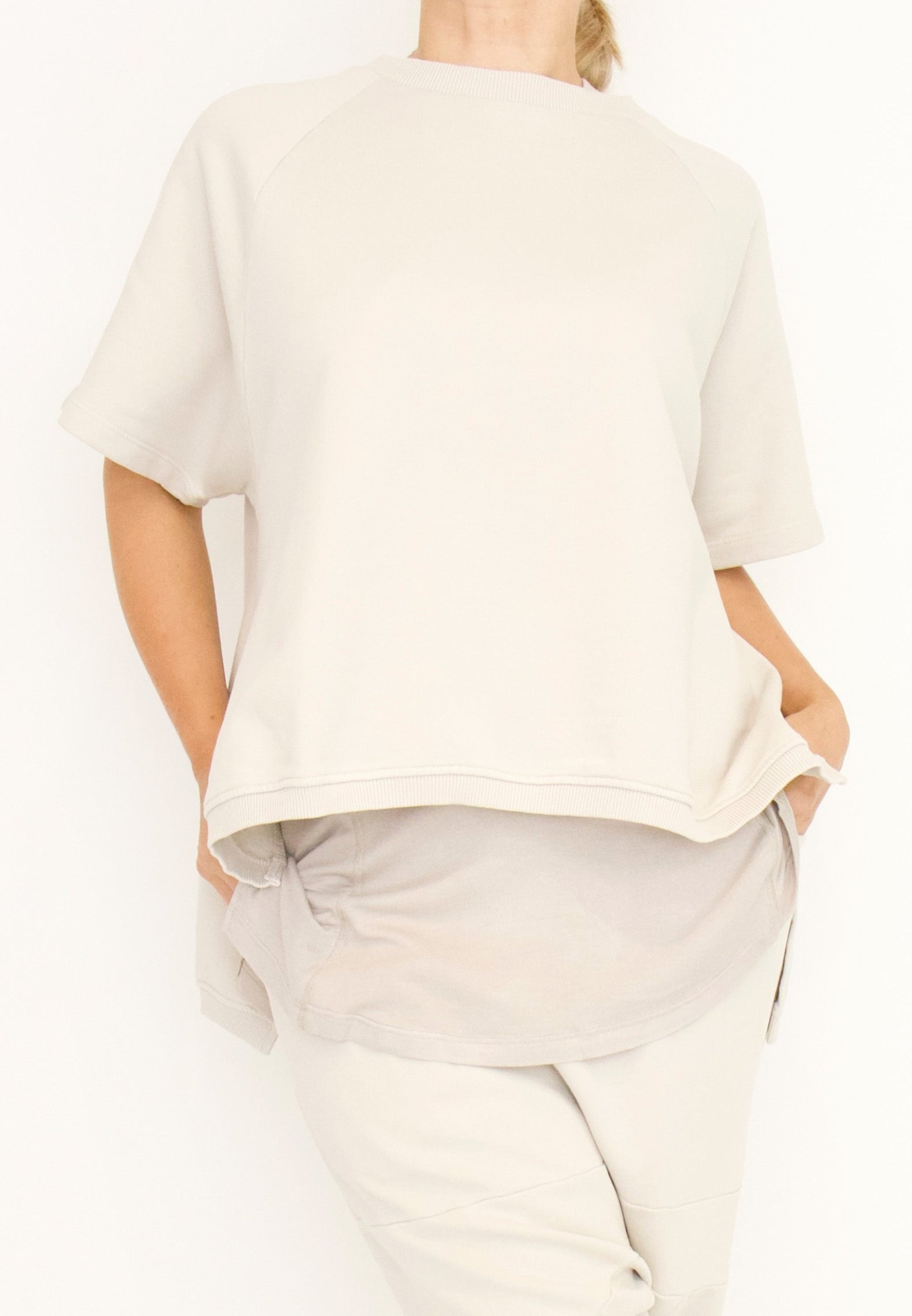 Women's short Ragland sleeve relaxed top, with a hi -low cut with 7" slits at the sides. Made in an organic cotton French Terry fabric from Sort Aarhus. In colour creme. Front view.