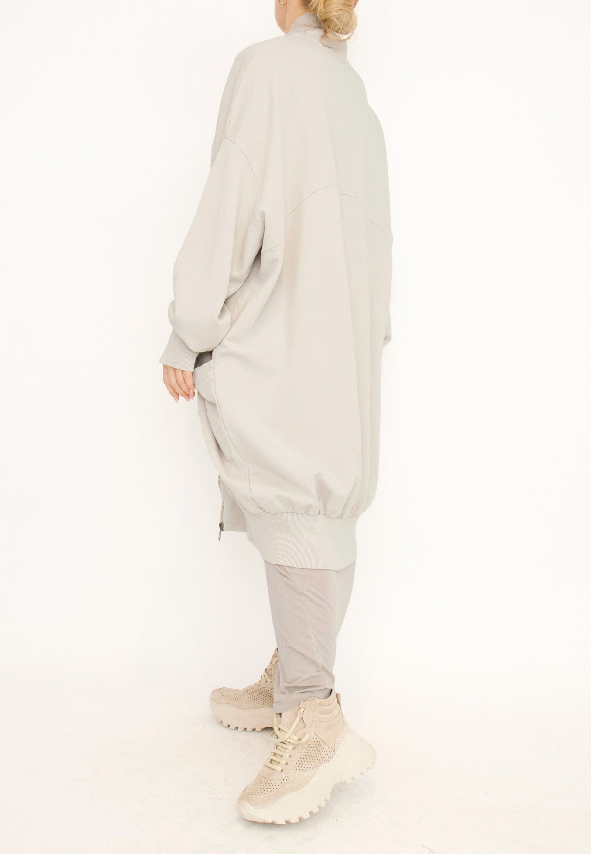 Women's long zip up cardigan, with long sleeves, ribbed collar, cocoon shaped silhouette and pockets. Made in French Terry fabric by Sort Aarhus. Colour creme. Side view.
