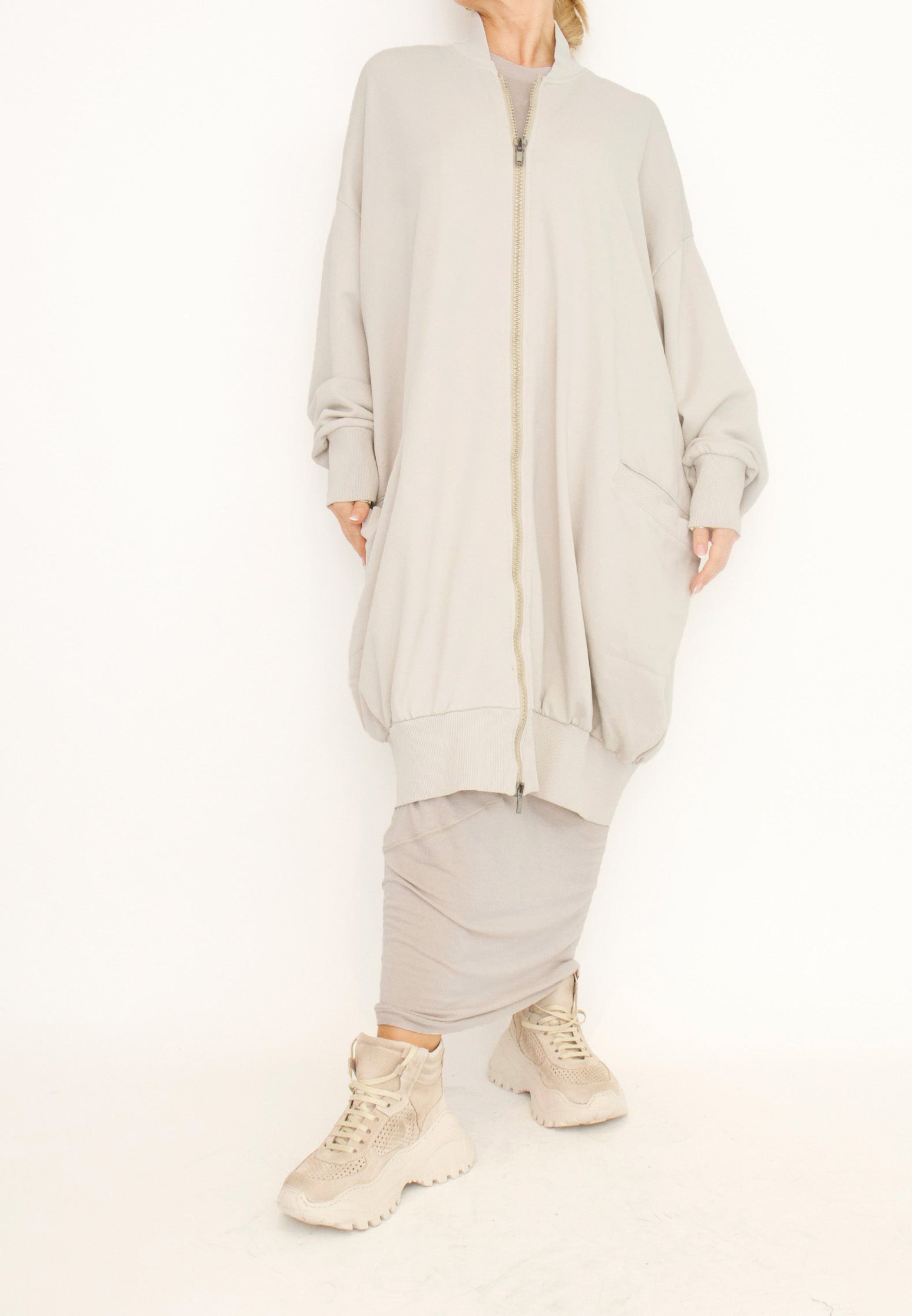 Women's long zip up cardigan, with long sleeves, ribbed collar, cocoon shaped silhouette and pockets. Made in French Terry fabric by Sort Aarhus. Colour creme. Front view.